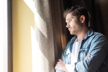 Side view of displeased man with crossed arms looking at window at home