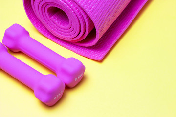 Pink sports mat and dumbbells on a yellow background, a copy of the space