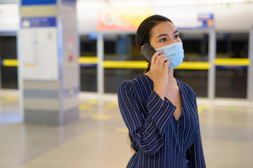 Young Asian businesswoman with mask talking on the phone at the subway train station