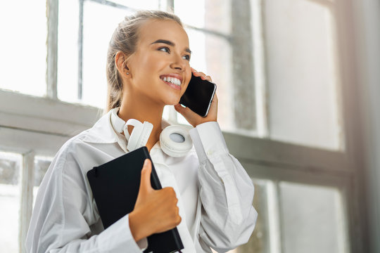 Smiling girl talking on smartphone, holding black notepad. Beautiful girl use mobile phone for work, call clients