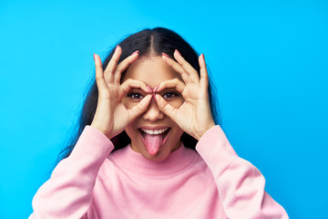 Funny black woman showing tongue and lmaking eyewear with fingers on blue background