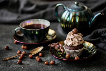 still life with cupcake on a saucer on a dark background, beautiful tea service, scattered hazelnuts, flatlay with a sweet dessert
