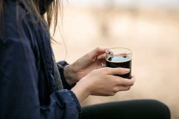 girl holding a transparent cup with a black drink, coffee, cola or kvass
