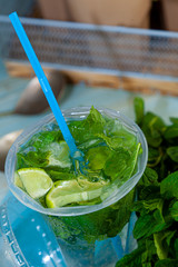 Mojito and Lemonade summer cold drink in a plastic glass with a straw. Coctail with mint, lemon, lime and ice. Serve at the bar. Beverage closeup.