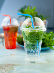 Mojito and Lemonade summer cold drink in a plastic glass with a straw. Coctail with mint, lemon, lime and ice. Serve at the bar. Beverage closeup.