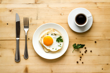 Fried eggs sandwich on plate - light wooden dinner table top view