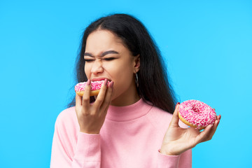 Hungry pretty girl eating donuts isolated over blue background