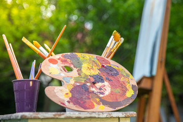 painter's wooden palette stained with a mess of fresh mixed colorful oil paints, rests on easel after artistic painting plainair, creative disorder