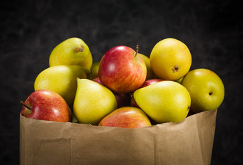 apples and pears in a paper bag of craft paper on a dark background