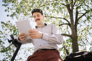 View from bottom of boy with moustache using tablet. Bottom view of man with moustache holding tablet while sitting under tree and propping himself up on rudder.