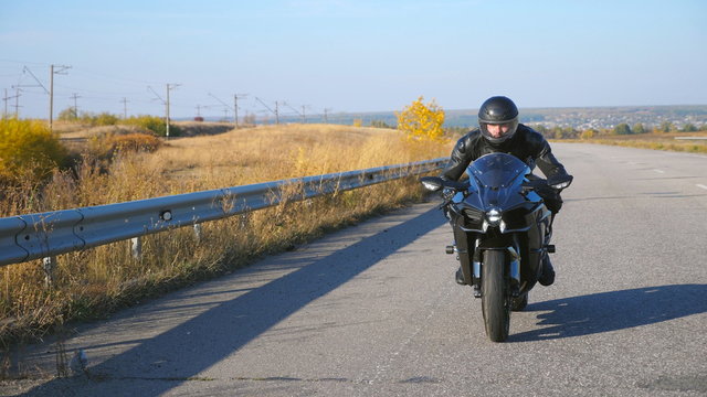 Young Man Riding On Modern Sport Motorbike At Autumn Highway. Motorcyclist Racing His Motorcycle On Country Road. Guy Driving Bike During Trip. Concept Of Freedom And Adventure.Front View Slow Motion