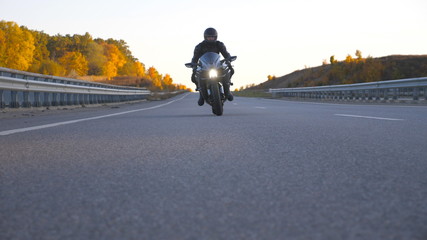 Front view of young man in helmet riding fast on modern sport motorbike at highway. Motorcyclist racing his motorcycle on country road. Guy driving bike during trip. Concept of freedom and adventure