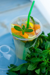 Mojito and Lemonade summer cold drink in a plastic glass with a straw. Coctail with mint, lemon, lime and ice. Serve at the bar. Beverage closeup.