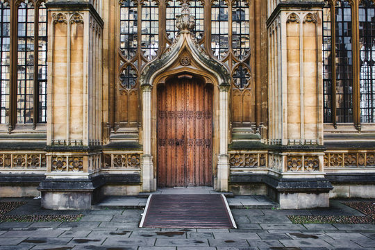 Exterior of the Divinity School in Oxford showing a big wooden door entrance and columns and stained glass windows