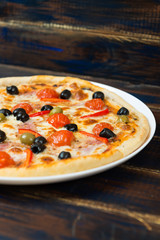 Fresh pizza with tomato sauce, black olives, mozzarella cheese, ham on wooden table closeup