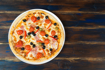 Fresh pizza with tomato sauce, black olives, mozzarella cheese, ham on wooden table closeup