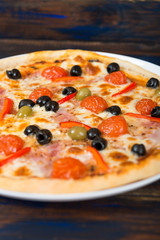 Fresh pizza with tomato sauce, black olives, mozzarella cheese, ham on wooden table closeup