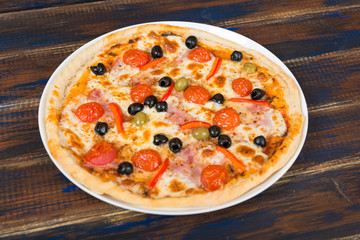 Fresh pizza with tomato sauce, black olives, mozzarella cheese, ham on wooden table closeup