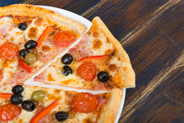 Fresh pizza with tomato sauce, black olives, mozzarella cheese, ham on wooden table closeup