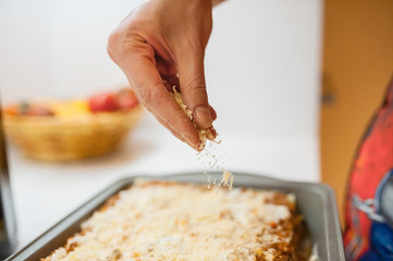 The cook sprinkles grated cheese on the dish. We stay at home and cook lasagna.