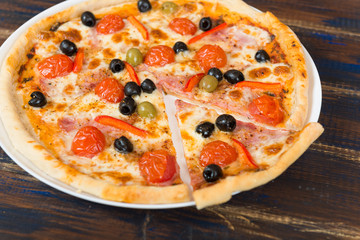 Fresh pizza with tomato sauce, black olives, mozzarella cheese, ham on wooden table closeup