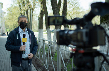 Fototapeta na wymiar A middle- aged European journalist in a protective medical mask is reporting in a deserted city.