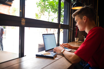 Hipster guy editing web site via laptop computer while sitting in coffee shop. Man marketing coordinator distance working on notebook gadget during rest in cafe