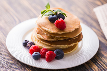 Pancakes with blueberries and raspberry on wooden background. Breakfast and traditional meal.