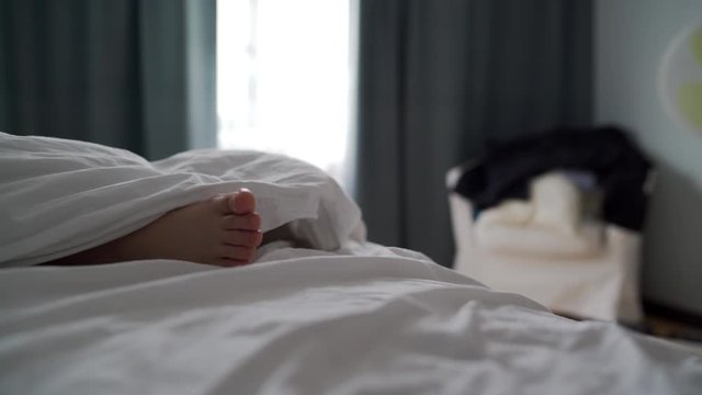 Woman sleeping in bed in the morning at home, beautiful female bare foot under white blanket closeup.