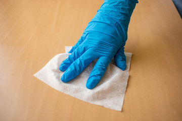 Woman cleaning home office wood table sanitizing surface with wet wipes in blue gloves stock photo