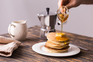 Maple syrup pouring over a stack of mini pancakes.