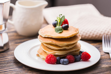 Pile of pancakes with blueberries and raspberries for breakfast on wooden table.
