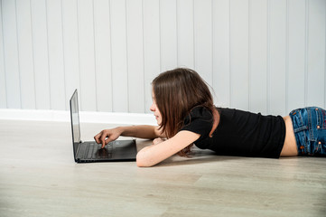 A teenage girl  on the background of light wall with a computer
