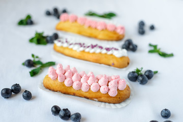 Tasty homemade eclairs on a white tablecloth. Blueberries are scattered everywhere.