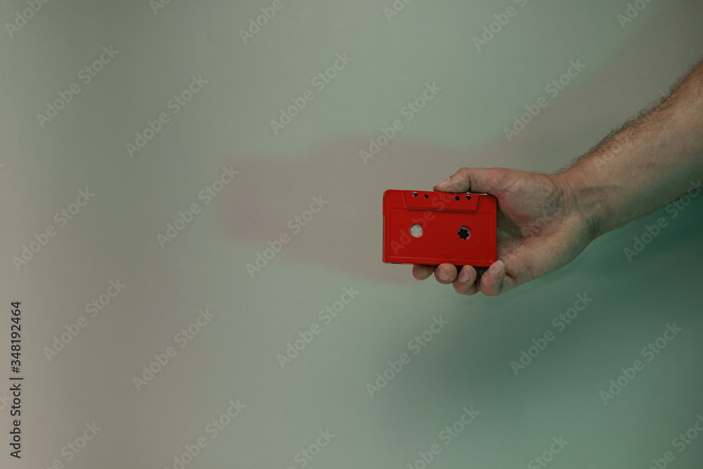 Poster Hand holding red audio cassette tape in the color light. Beautiful minimal in neon light. Minimalism retro style concept. Background pattern for design.