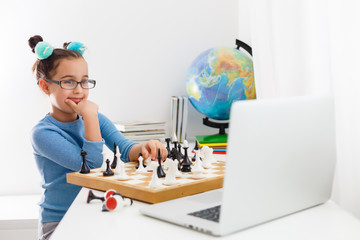 Portrait Caucasian Little cirly girl playing chess at the table in interior with chessboard. little...