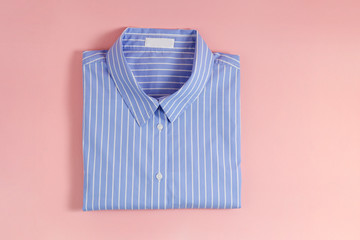 One perfectly folded buttoned shirt with striped pattern. Single piece of formal wear with blank label isolated on pink background. Close up, top view, copy space. - obrazy, fototapety, plakaty