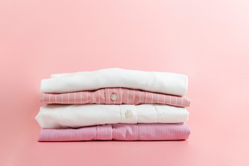 Stack of colorful perfectly folded clothing items. Pile of different pastel color shirts and sweaters isolated on pale pink background. Close up, top view, copy space.