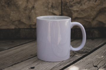 White Coffe mug with no design outside over the wood tablewith the blured background, perfect for business. Can be used for muck-ups and used your design