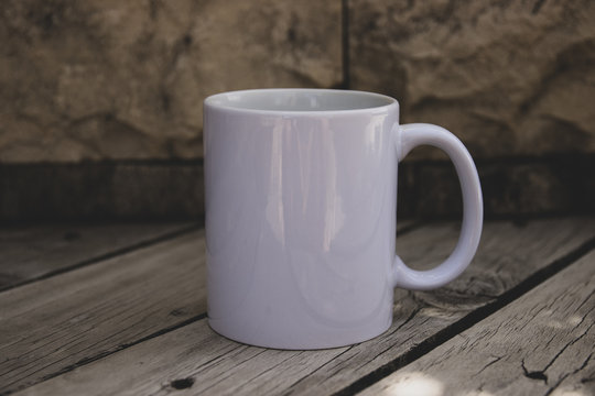 White Coffe mug with no design outside over the wood tablewith the blured background, perfect for business. Can be used for muck-ups and used your design