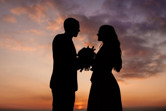 silhouettes of the bride and groom, the newlyweds look at each other holding a wedding bouquet in their hands. Wedding photography concept.