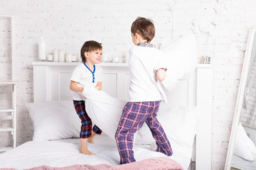 Obraz na płótnie Canvas Two brothers boys, siblings in pajamas making pillow fight in bed