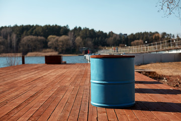 Naklejka premium The blue barrel stands on the lake shore on a wooden pier. Spring landscape, blurred background