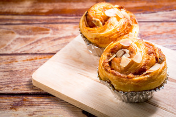 Delicious homemade almond danish bread in foil cup on a wooden table in the home kitchen on black background.
