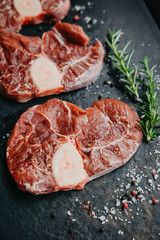Raw beef steak osso bucco with herbs and spices on dark table. Marble meat. Top view and copy space