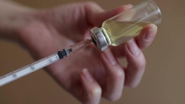 Female hands inject the solution into a vial of vaccine with a syringe