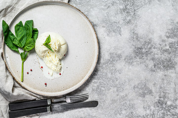 Mozzarella Burrata cheese on a white plate with Basil leaves. Gray background. Top view
