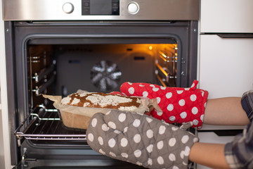 Housewife hands in oven mitts takes out fragrant and crunchy bread from the oven in the kitchen. Homemade fresh bread without yeast. - 348201497