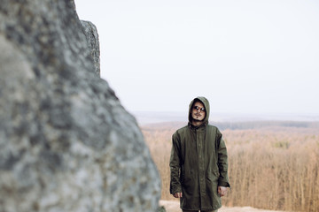 A young man in a hood stands near a high cliff. Travel concept