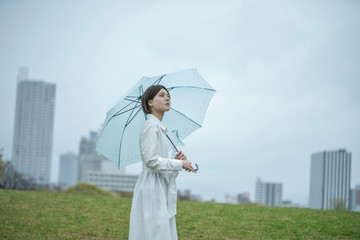 雨の中傘を挿して佇む白いワンピースを着た若い女性
